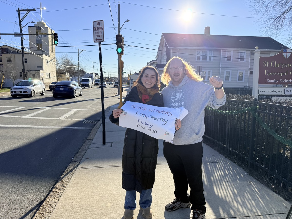 Two Good Neighbors volunteers outside St. Chrysostom's holding a pantry-day sign